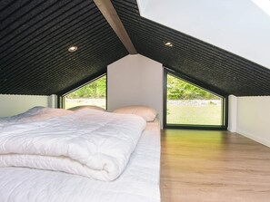 Ein Schlafzimmer mit schräg versetzter Decke, einem Bett mit weißer Bettwäsche und Blick ins Grüne.