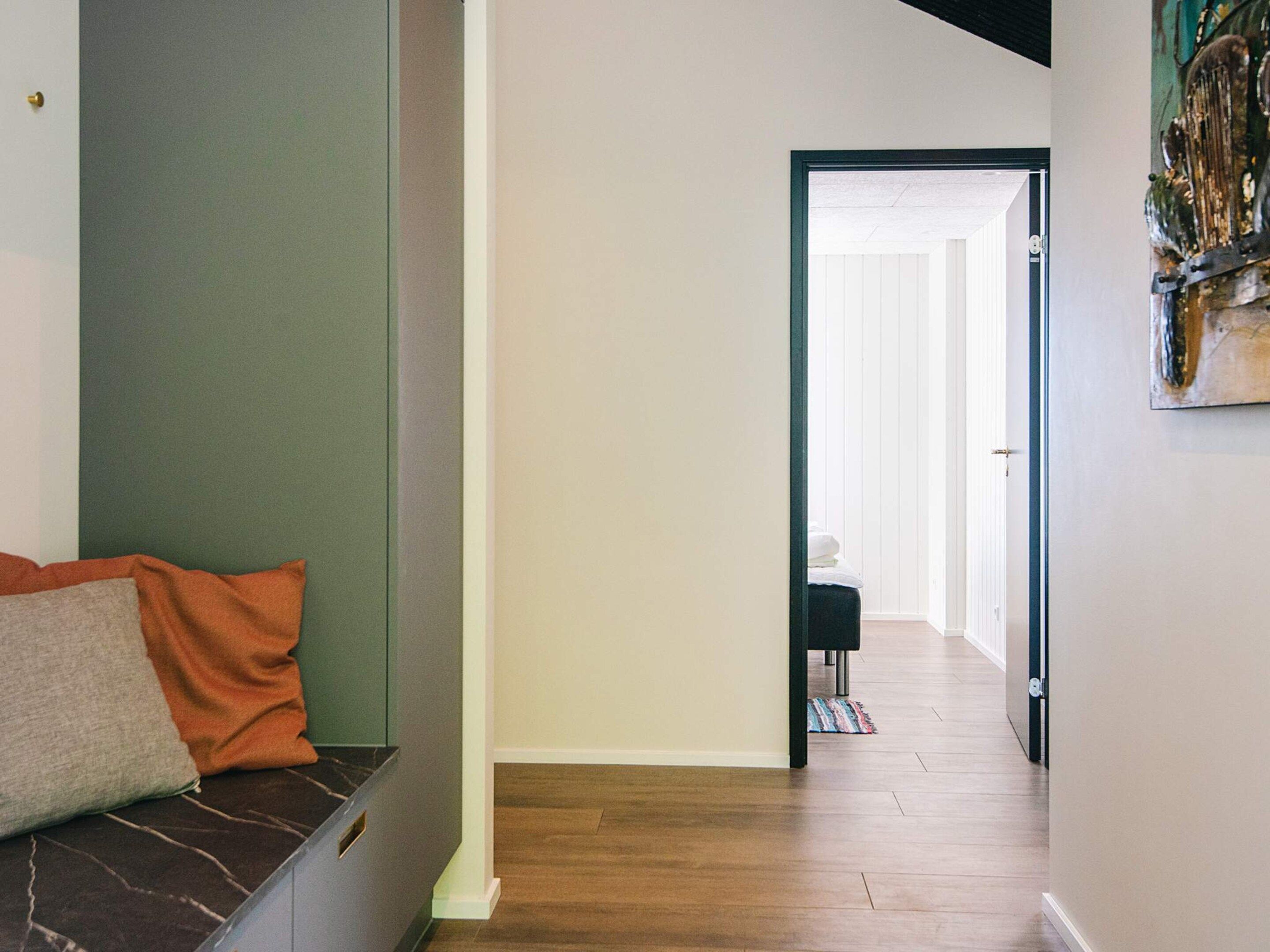 A hallway with a bench, a door leading to another room, and a painting on the wall.