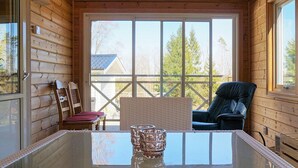 Une cabane en bois avec une table à plateau de verre, deux chaises et une vue sur une maison, visible à travers de grandes fenêtres.