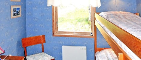 A bedroom with a bunk bed, a chair, a desk, a radiator, and a window with a curtain.