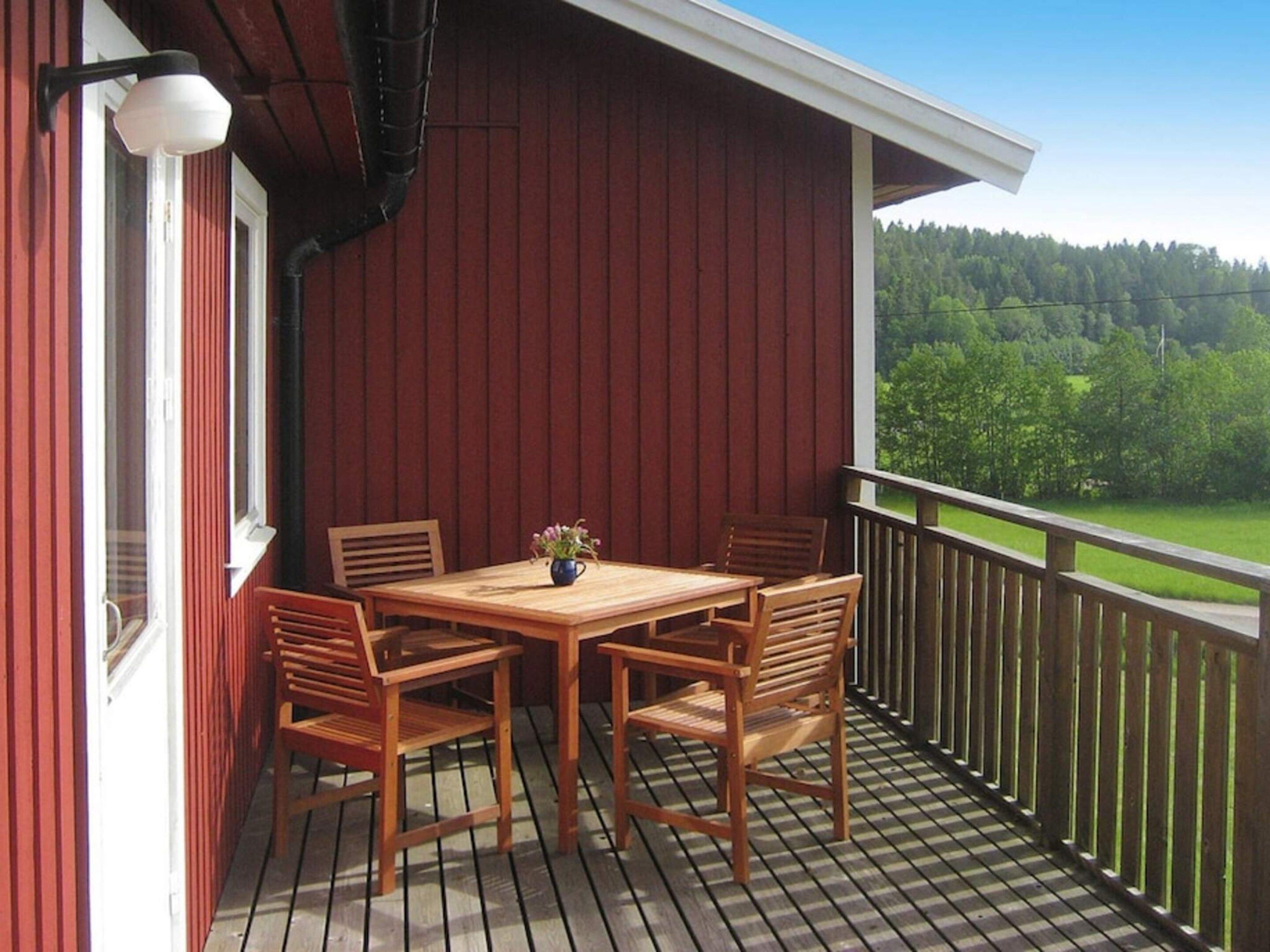 En træterrasse med et bord og stole, en plantekasse og udsigt til et skovområde.