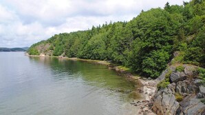 A natural landscape with a calm body of water, a rocky shoreline, and dense greenery. - 4 Person Holiday Home in Henan (Henån)