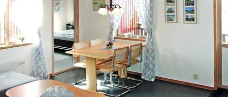 A room with a dining table, chairs, a sofa, a bed, and a window with curtains.