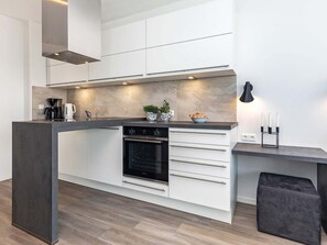 A modern kitchen with a built-in oven, a coffee maker, and a small island with a sink. - 5 Star Holiday Home in Wendtorf (Wendtorf)