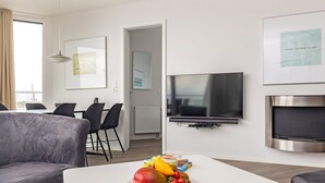 Una sala de estar moderna con un televisor de pantalla plana, un comedor con sillas y un plato de fruta sobre una mesa de centro.