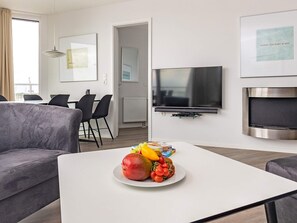 A modern living room with a flat-screen TV, a dining area with chairs, and a fruit plate on a coffee table. - 5 Star Holiday Home in Wendtorf (Wendtorf)