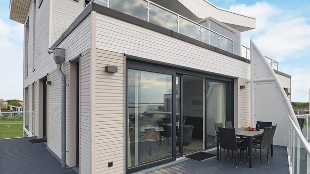 Una casa moderna con terraza, puerta corrediza de vidrio que da a una sala de estar y escalera a un nivel superior.