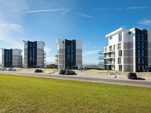 Et moderne lejlighedskompleks med flere bygninger, en parkeringsplads og en græsplæne foran.