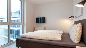 A modern bedroom with a large window, a flat-screen TV, and a bedside lamp.