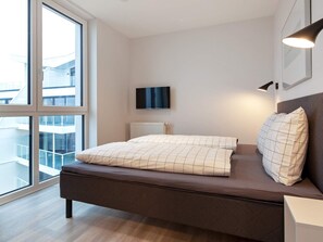 A modern bedroom with a large window, a flat-screen TV, and a bedside lamp.