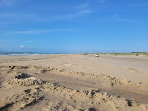 A wide, open beach with a white car parked on the sand, a clear blue sky, and a distant view of the ocean. - 5 Star Holiday Home in Lokken (Lokken)