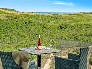 A table with a bottle and glasses, overlooking a green landscape with dunes.