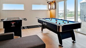 Et billardbord, en dartskive og et fodboldbord i et rum med store vinduer.