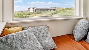 Et værelse med seng, puder og et vindue med udsigt til et hus og landskab.