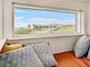 A room with a bed, pillows, and a window overlooking a house and landscape. - 5 Star Holiday Home in Lokken (Lokken)
