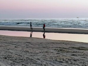 A beach with a calm sea, a boat in the distance, and footprints in the sand.