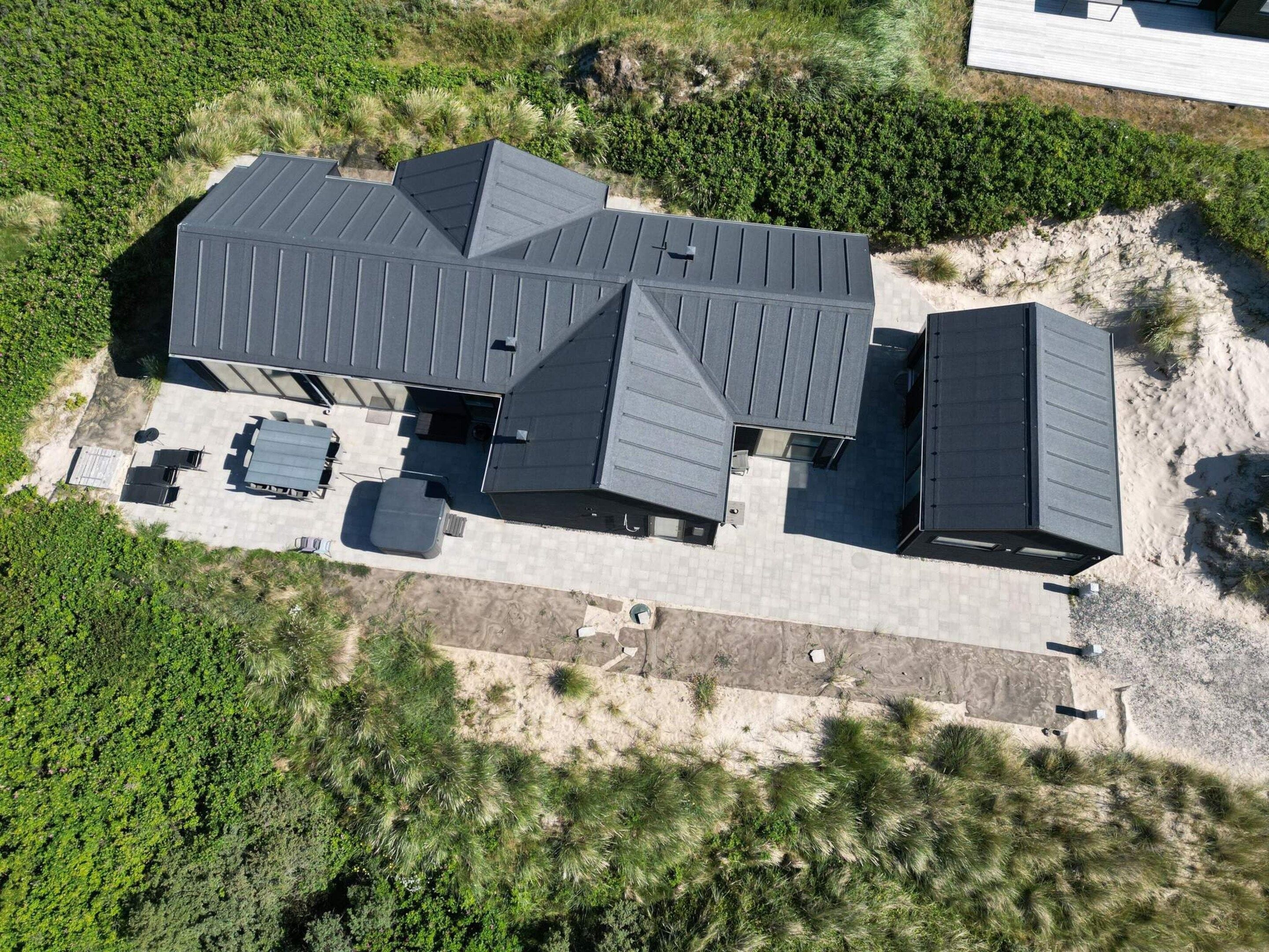 A modern house with a flat roof, a patio area with outdoor furniture, and a well-maintained garden.