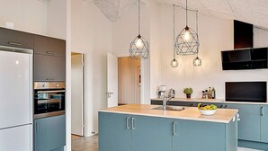 Et moderne køkken med en central ø, indbyggede hårde hvidevarer og hængende lamper.