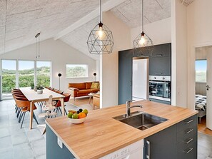 Une cuisine moderne dotée d’un îlot central, d’un coin repas avec une table et des chaises, et offrant une vue sur l’extérieur.