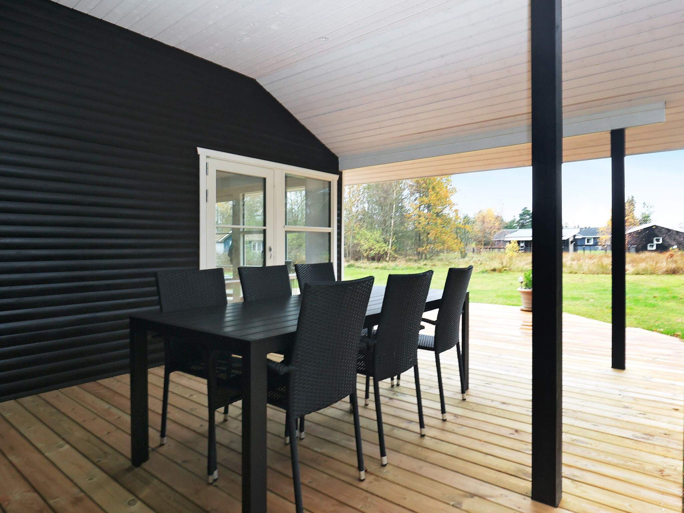 A covered outdoor dining area with a table and chairs, a view of the surrounding landscape, and a door leading to the interior.