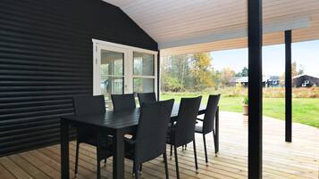 A covered outdoor dining area with a table and chairs, a view of the surrounding landscape, and a door leading to the interior.
