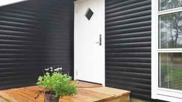 A wooden platform with a potted plant in front of a white door with a small window.