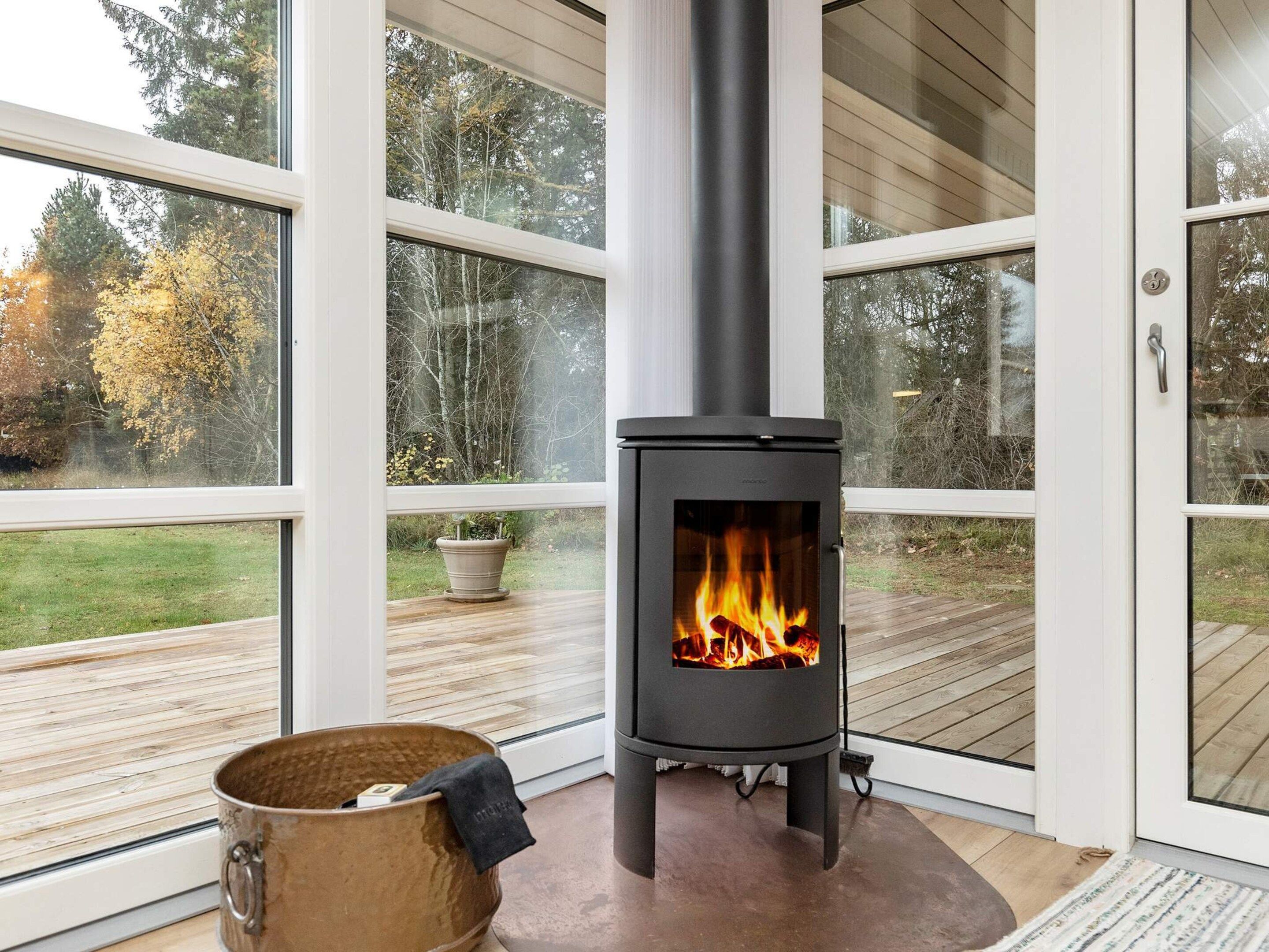 A modern interior with a wood-burning stove, large windows, and a wooden deck.