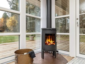 Un intérieur moderne agrémenté d’un poêle à bois, de grandes fenêtres et d’une terrasse en bois.