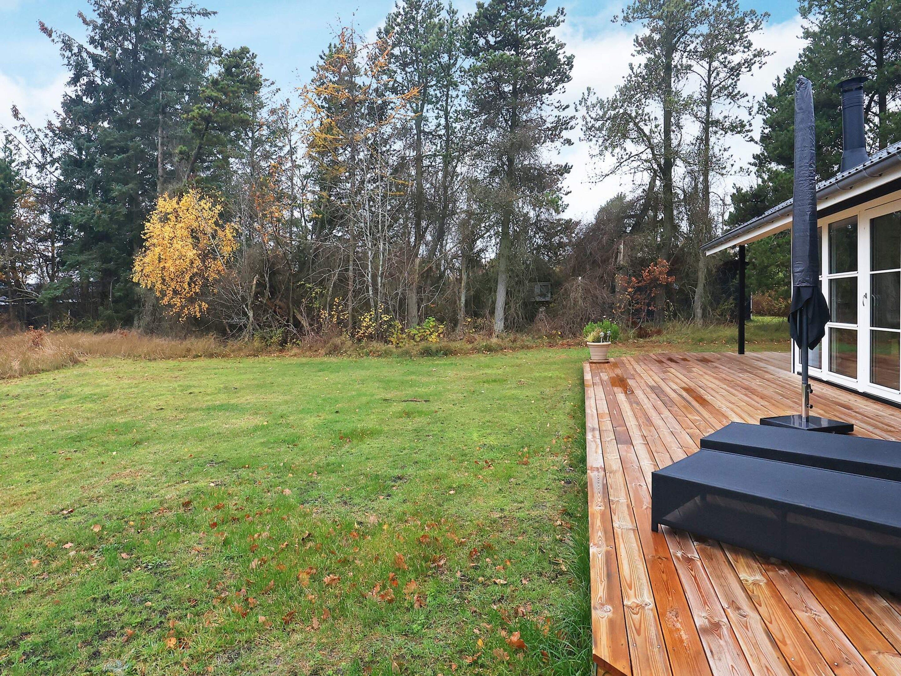 A wooden deck with a black outdoor seating area, surrounded by a grassy yard and trees.