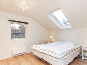 Un dormitorio con techo inclinado, tragaluz, cama, mesita de noche con lámpara y ventana.