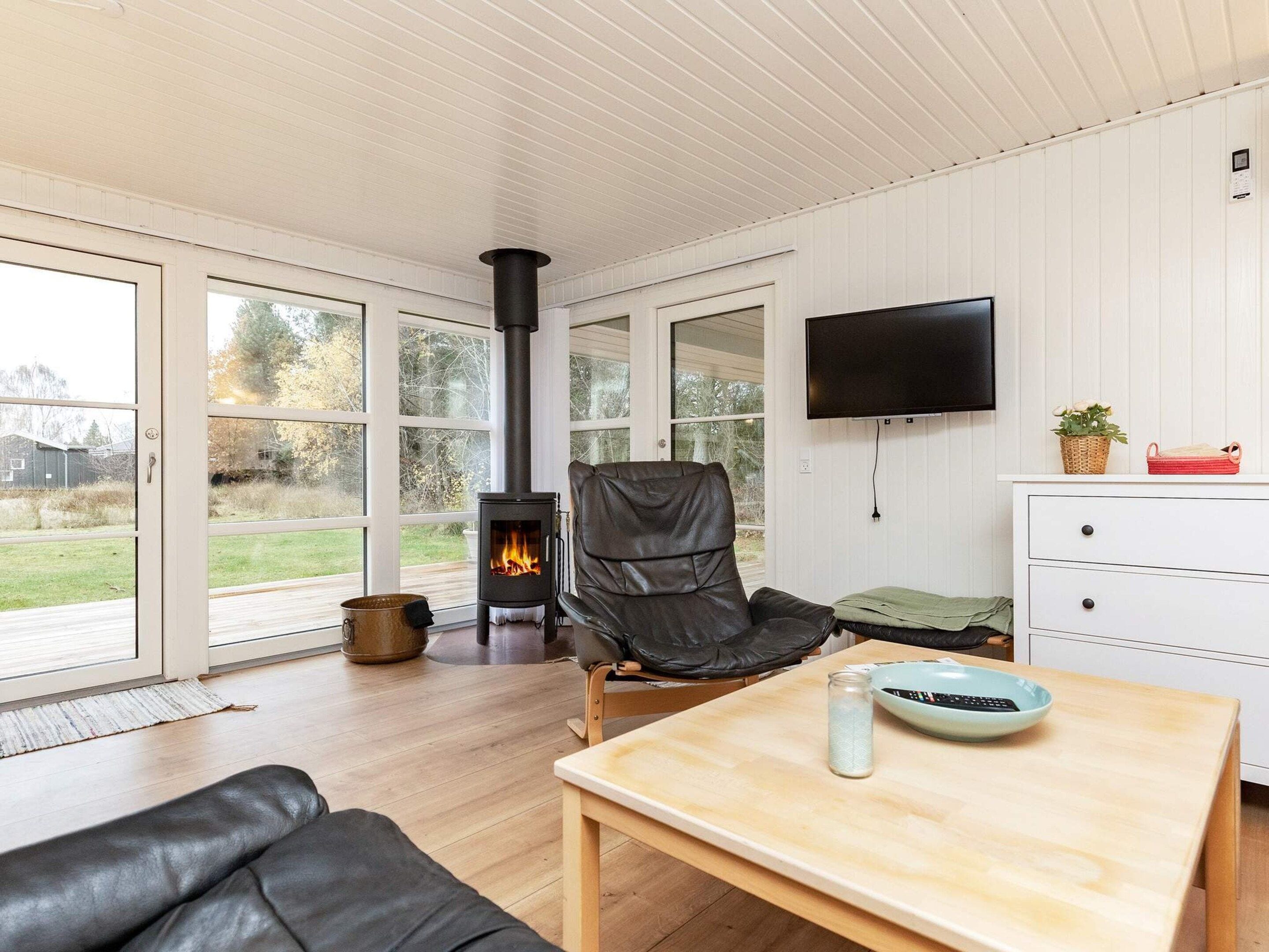 A modern living room with a fireplace, a leather chair, a wooden table, and a TV mounted on the wall.