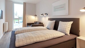 Quarto moderno com uma cama grande, um sofá e vista para o exterior.