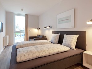 A modern bedroom with a large bed, a sofa, and a view of the outdoors.
