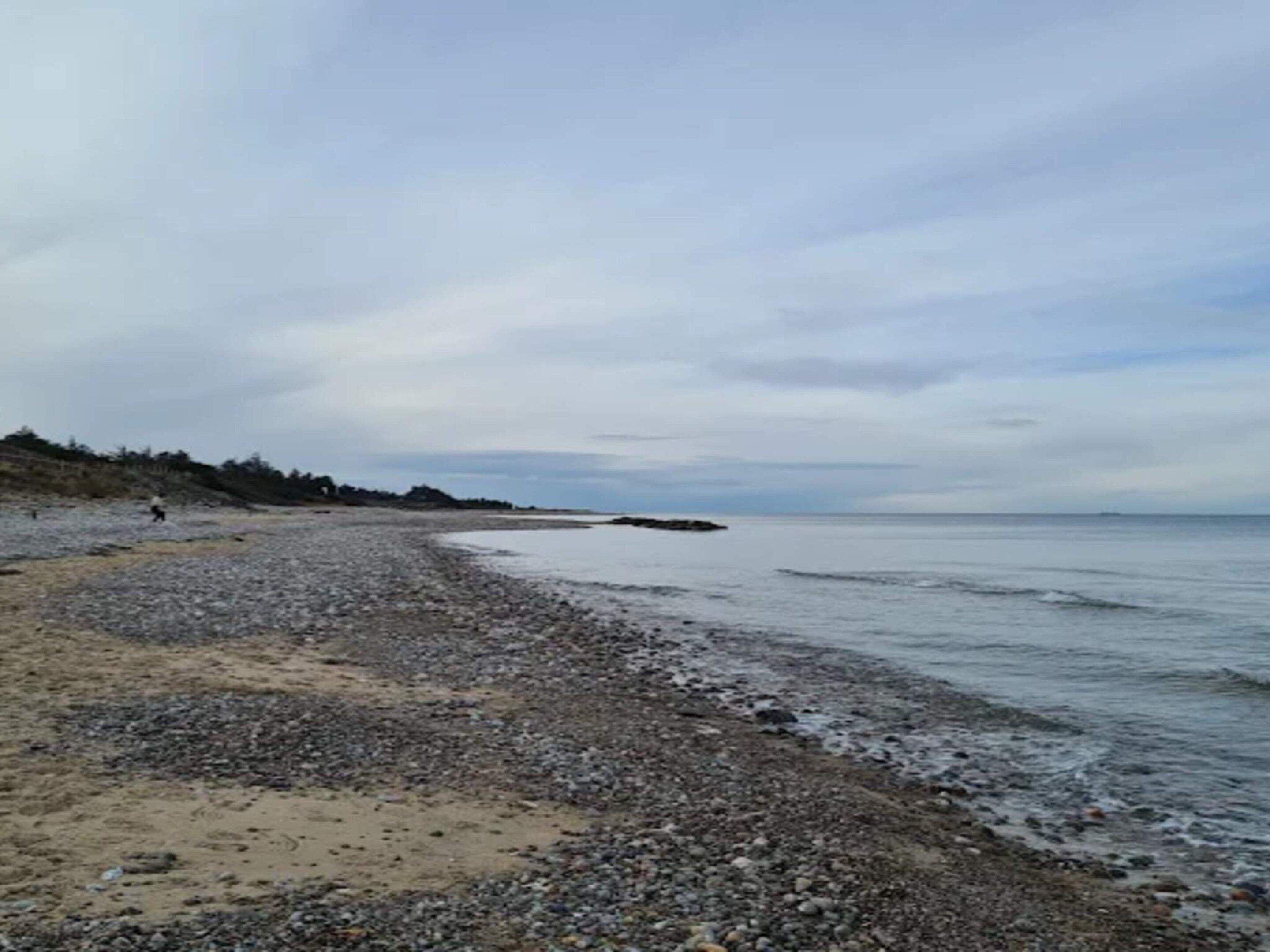 A pebbly beach with a rocky shoreline and a distant view of the sea.