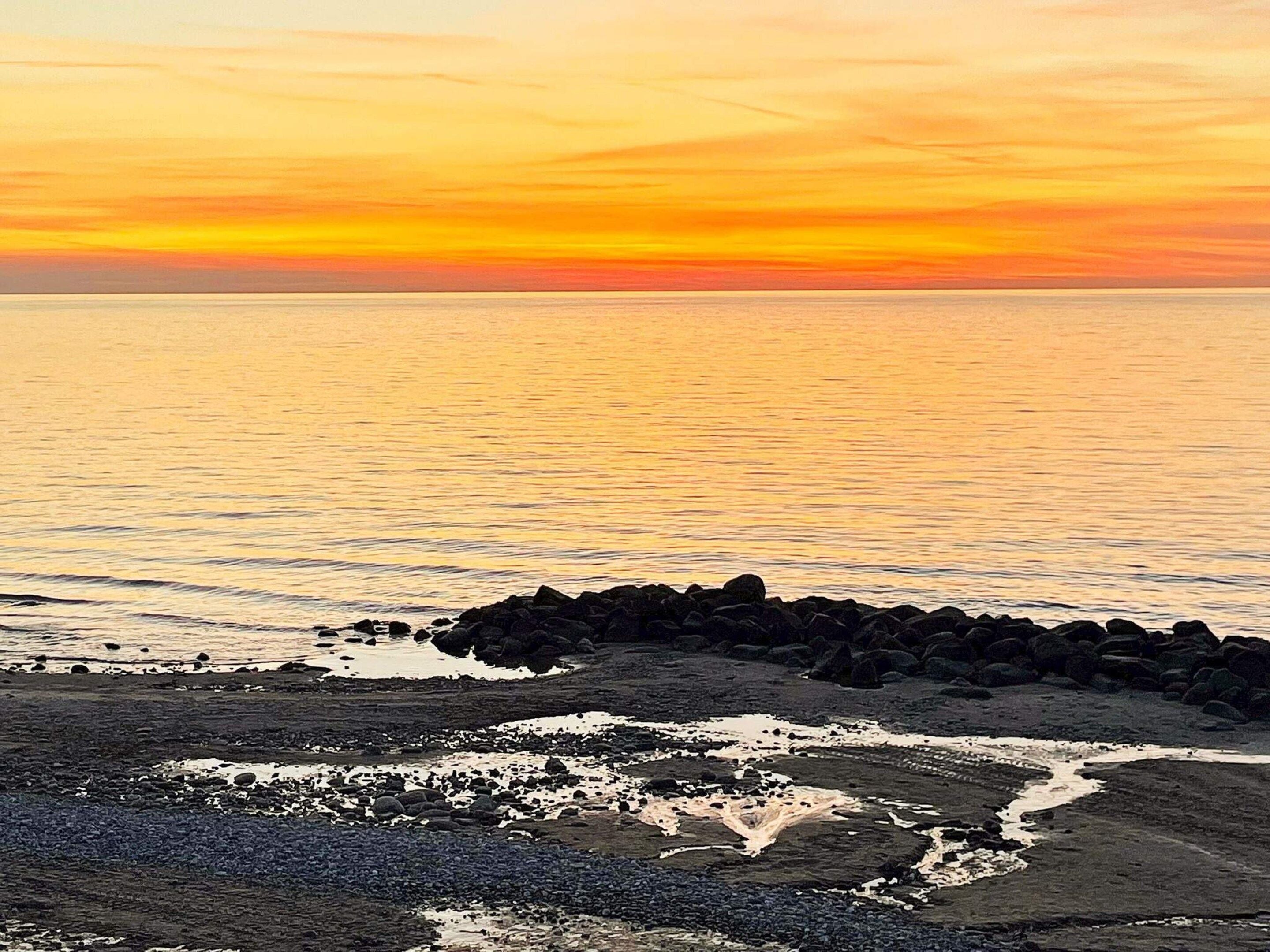 Een kustlandschap met een rotsachtige kustlijn en een rustige zee tijdens zonsondergang.