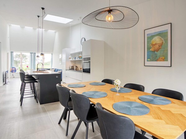 Une cuisine moderne avec un coin repas, comprenant un îlot central, des luminaires suspendus et une grande fenêtre.