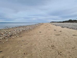 A sandy beach with pebbles and footprints leading to the water.