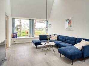 Un salon moderne avec un canapé d’angle, une table basse ronde et une vue sur l’extérieur.