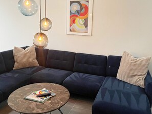 A modern living room with a dark blue sectional sofa, a round marble coffee table, and three hanging pendant lights.