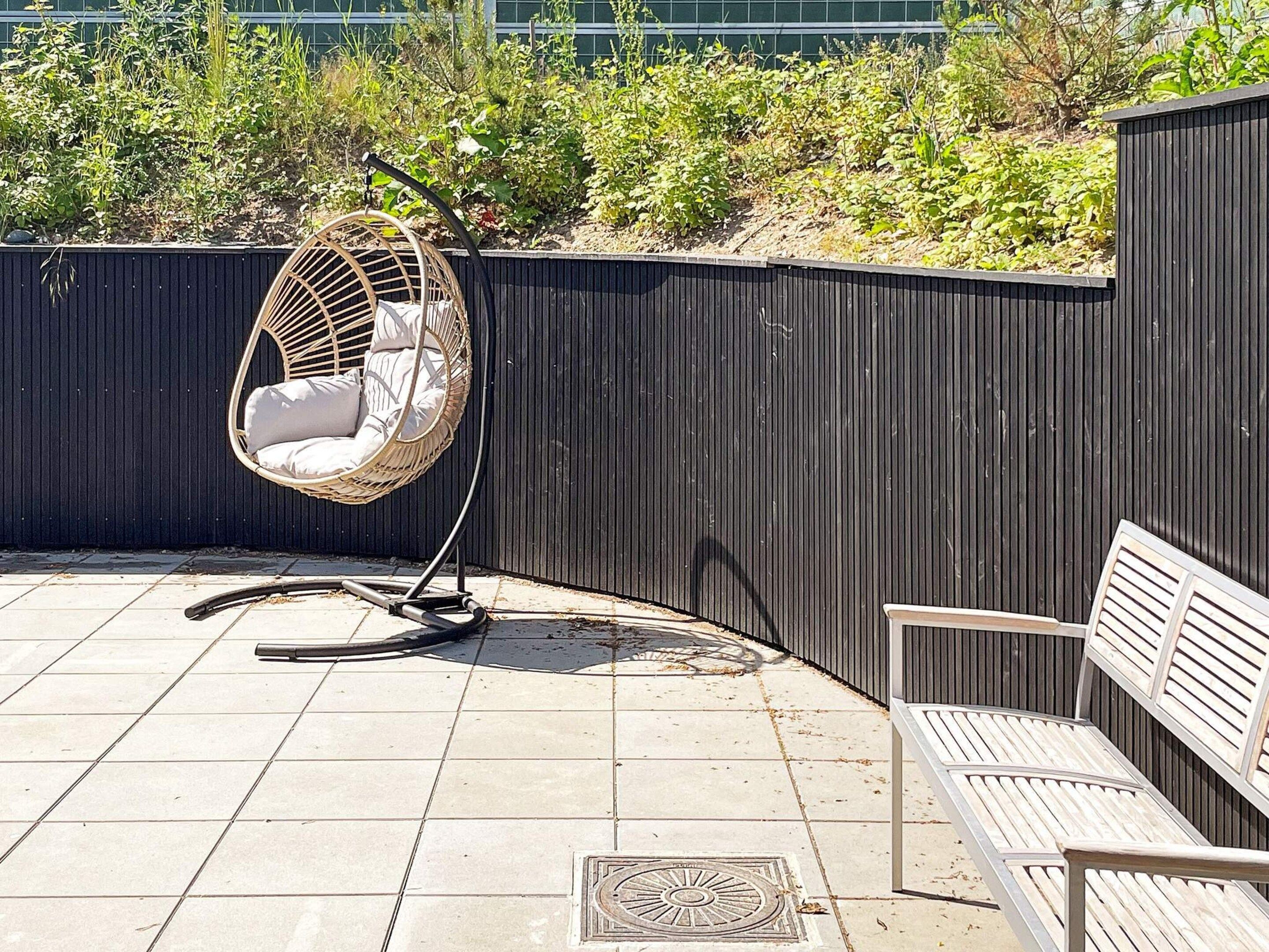 A patio area with a wicker hanging chair, a bench, and a tiled floor.