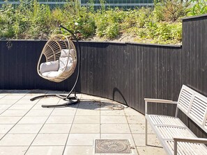 Un espace patio aménagé avec un fauteuil suspendu en osier, un banc et un sol carrelé.