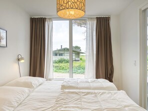 A bedroom with a bed, curtains, a lamp, and a view of a house through a window.