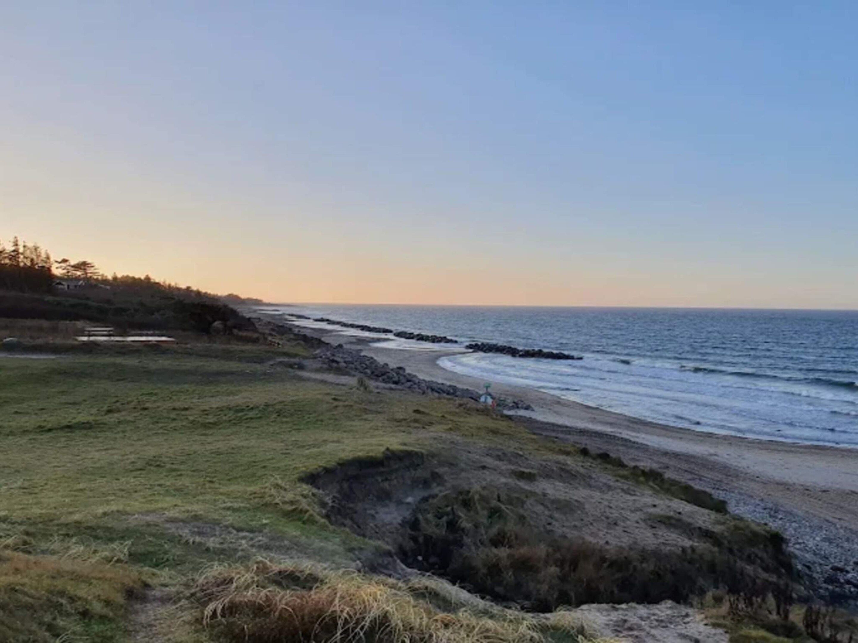 Un paysage côtier avec une zone herbeuse, une côte rocheuse et un ciel dégagé.