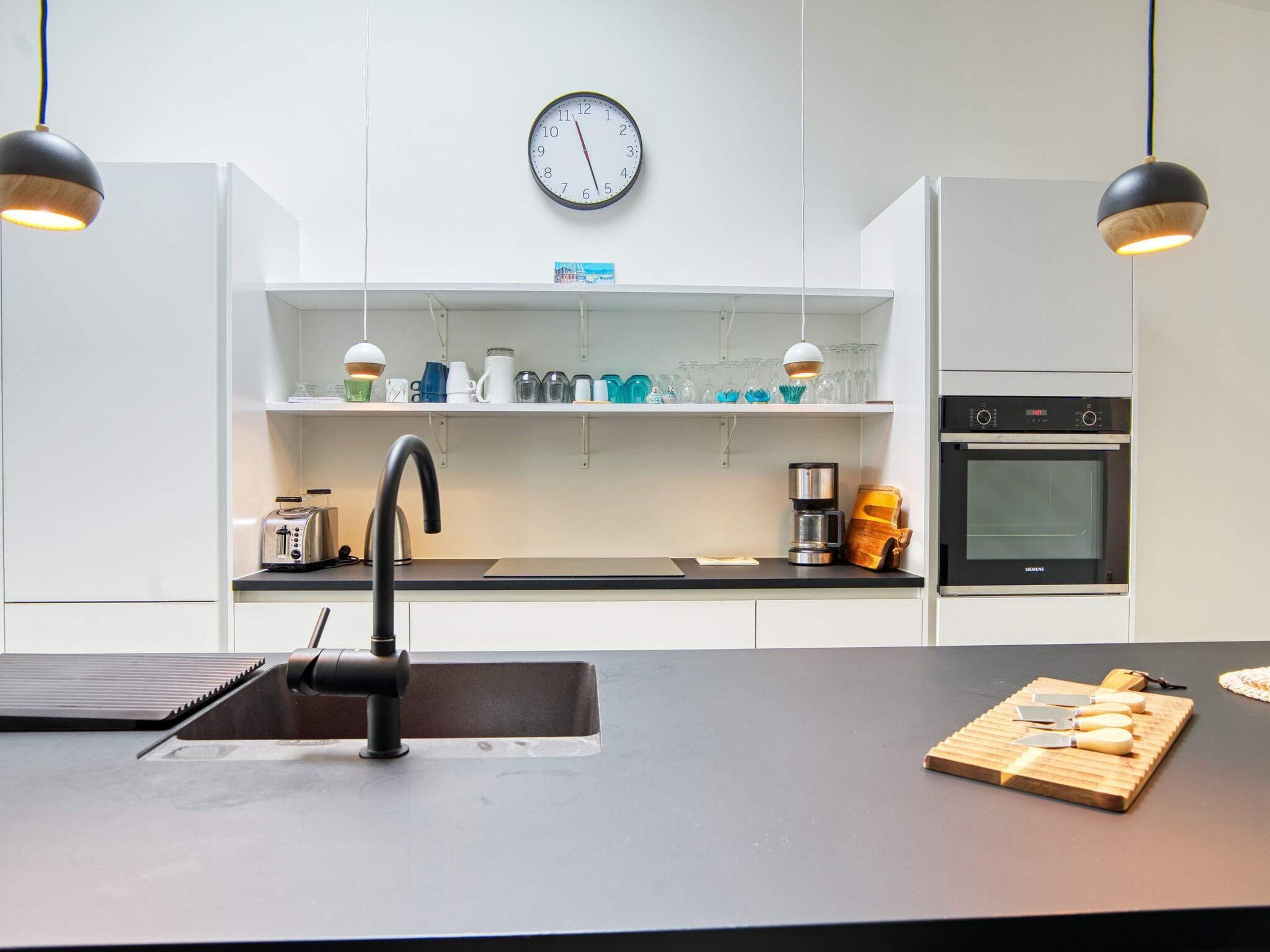 A modern kitchen with a black countertop, a sink, a clock, and a Siemens oven.