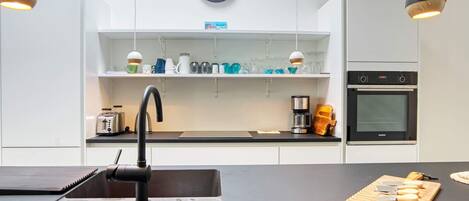 A modern kitchen with a black countertop, a sink, a clock, and a Siemens oven.