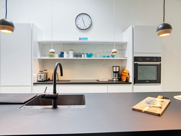 A modern kitchen with a black countertop, a sink, a clock, and a Siemens oven.