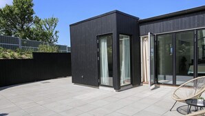 A modern building with a flat roof, large glass windows, and a paved patio area. - 6 Person Holiday Home in Gilleleje (Gilleleje)