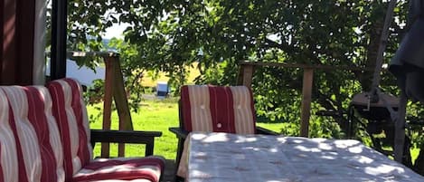 A cozy outdoor seating area with a sofa and chairs, a table, and a view of a lush garden.