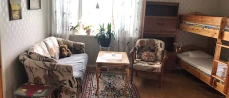 A cozy living room with a sofa, armchair, small table, and a bunk bed.