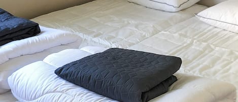 A bed with white bedding and a dark gray quilted pillow.